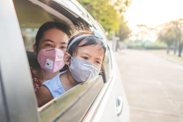 Mother and daughter in car wearing pm 2.5 face mask to protect against viruses and pollution