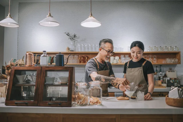 asian chinese senior male barista teaching his daughter making coffee at cafe bar counter