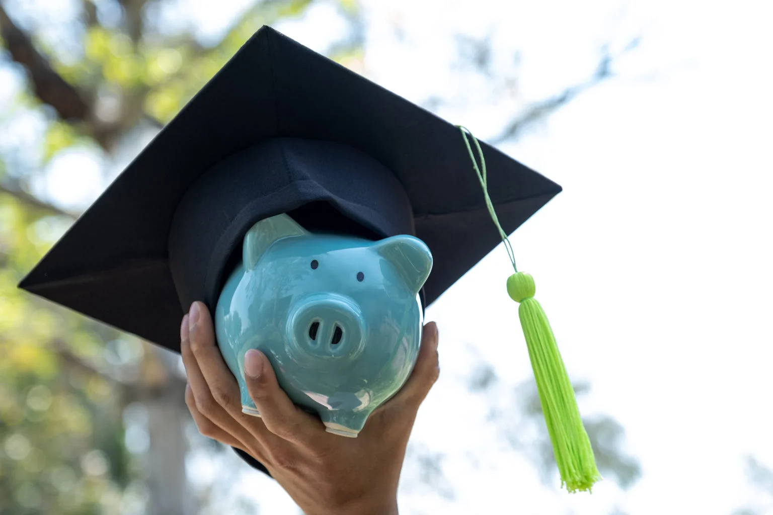 Hand holding Blue piggy bank with graduation hat, Saving money