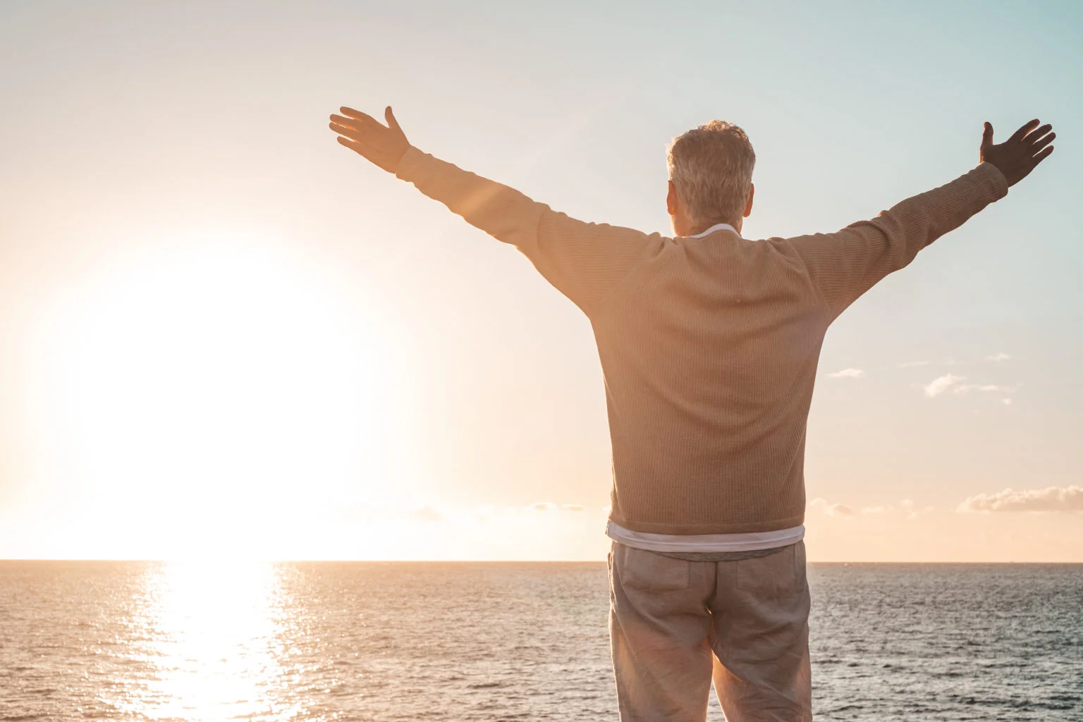 old man looking to the sunset and the sea with opened arms feeling free and happy