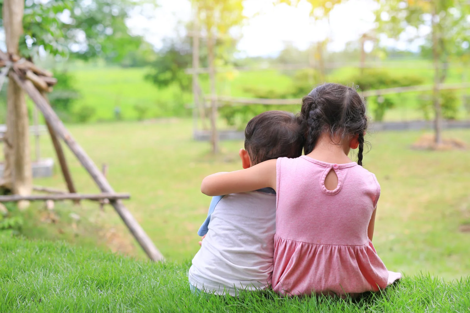 Older sister hugs little brother by the neck, shoulders sitting